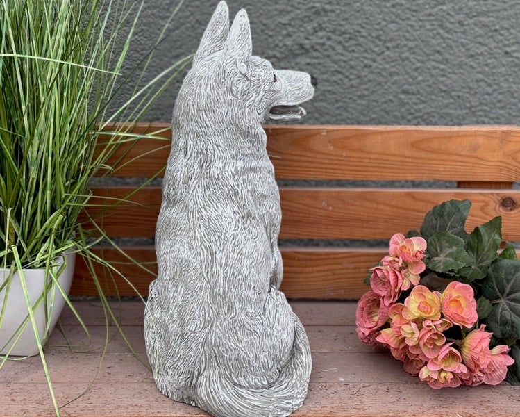 Gartenfigur Hund aus Steinguss, sitzend auf einer Holzbank neben Pflanzen.