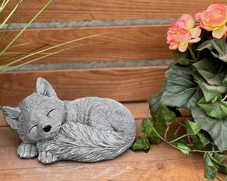 Schlafende Fuchs-Gartenfigur aus Stein auf einer Holzfläche neben einer Pflanze.
