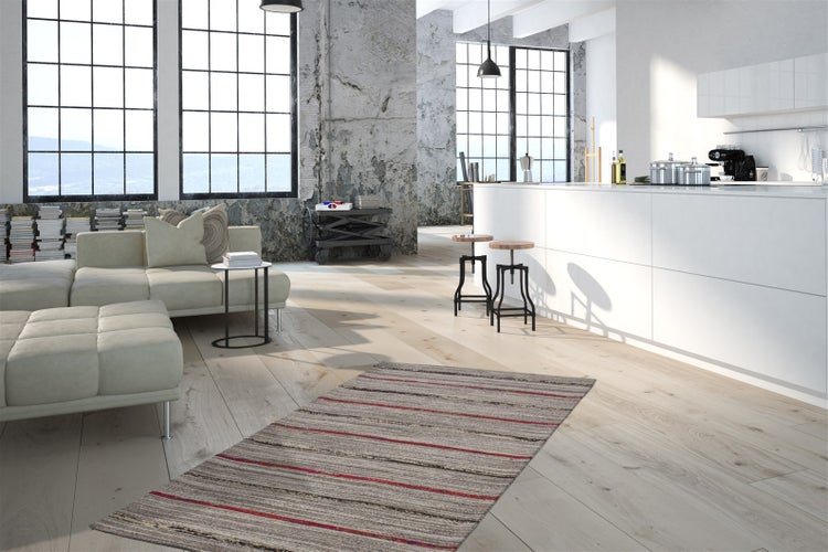 Heller Wohnbereich im Industriestil mit hellem Holzboden, einer Sichtbetonwand, einem Sofa und einer weißen Kücheninsel.