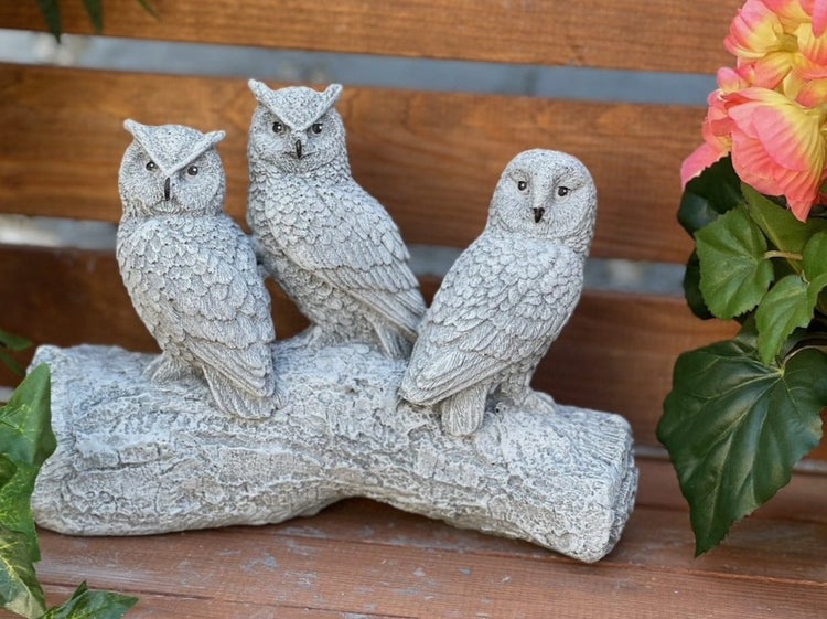 Drei steinerne Eulenfiguren sitzend auf einem Baumstamm als Gartendekoration