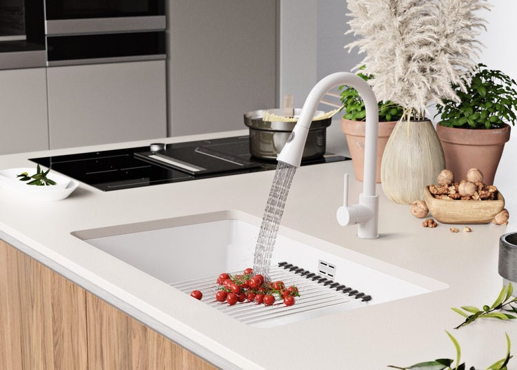 Küchenspüle mit Armatur, Tomaten und Abtropfgestell auf einer hellen Arbeitsplatte.