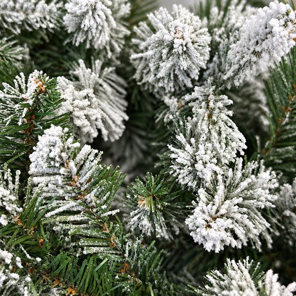 Detailansicht eines künstlichen Weihnachtsbaums mit beschneiten Tannenzweigen und Nadeln.