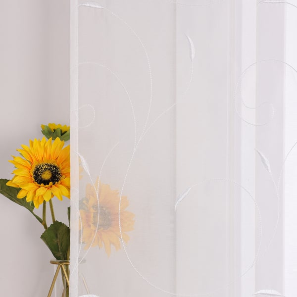 Gardine mit floralem Muster und Sonnenblumen im Hintergrund