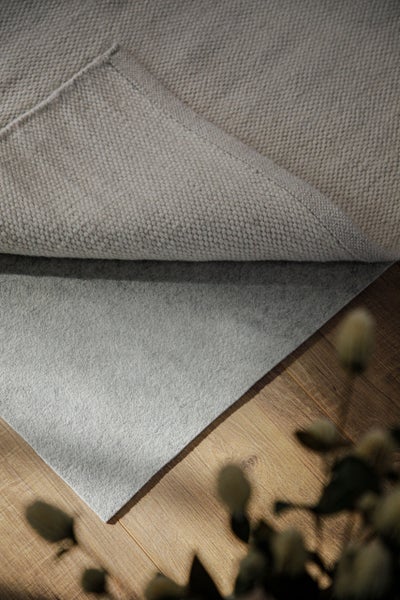 Teppichunterlage aus Filz unter einem gewebten Teppich auf einem Holzboden.
