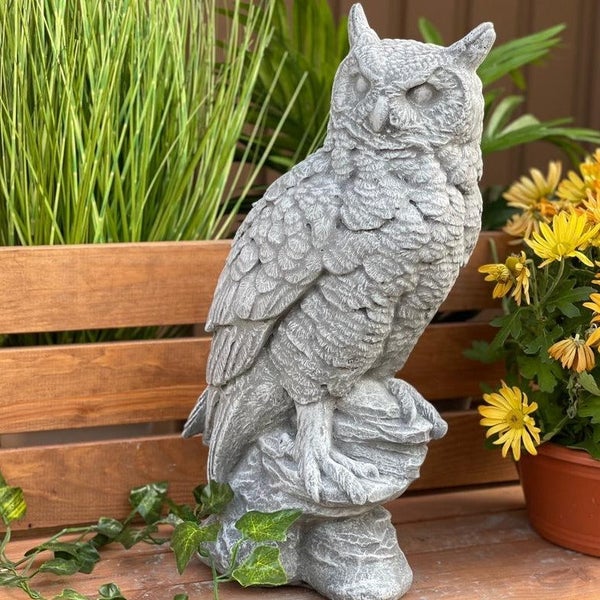 Steinfigur Eule als Gartenfigur aus witterungsbeständigem Material auf einem Holzuntergrund mit Pflanzen