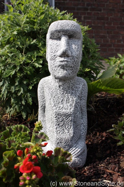 Gartenfigur Moai Kopf aus Steinguss in einem Blumenbeet.