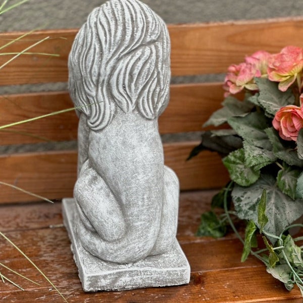 Gartenfigur sitzender Löwe aus Stein in der Rückansicht, platziert auf einer Holzbank neben Blumen.