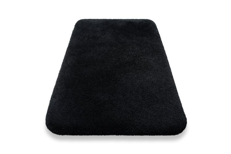 Schwarze rechteckige Badematte mit flauschiger Oberfläche und abgerundeten Ecken.