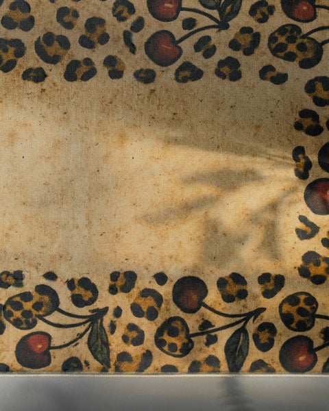 Dekorativer Teppich mit Leopardenmuster und Kirschen am Rand auf texturierter Oberfläche.