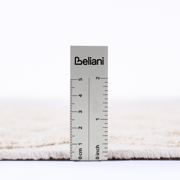 Detailaufnahme eines Teppichs mit einem Messlineal zur Messung der Florhöhe. Beliani Logo.