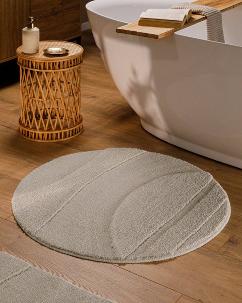 Runder Badteppich mit Reliefmuster aus weichem Material vor einer freistehenden Badewanne auf einem Holzboden.