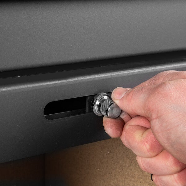 Detailansicht einer Hand, die einen silbernen Luftregler aus Metall an einem schwarzen Kaminofen einstellt.