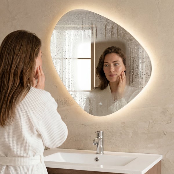 Organisch geformter Badezimmerspiegel mit LED Beleuchtung und Antifog Funktion über einem Waschbecken in modernem Badezimmer.