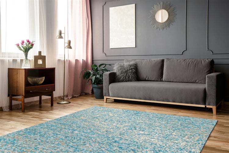 Modernes Wohnzimmer mit blau gemustertem Teppich auf hellem Holzboden, grauem Sofa, rosa Vorhängen und grauer Wand mit Zierleisten.