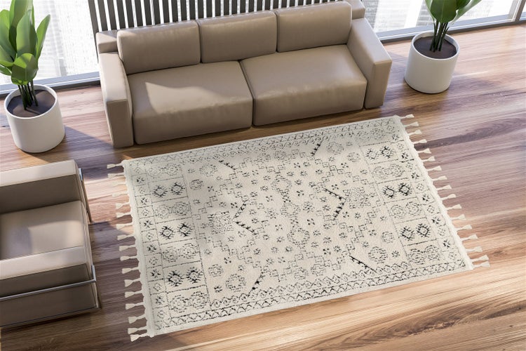 Helles Wohnzimmer mit Holzboden, beigem Sofa, Sessel, Pflanzen und einem cremefarbenen Teppich mit schwarzen geometrischen Mustern und Fransen.