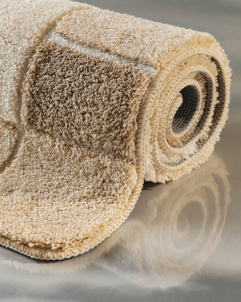 Zusammengerollte beige Badematte mit hohem Flor und Karomuster.