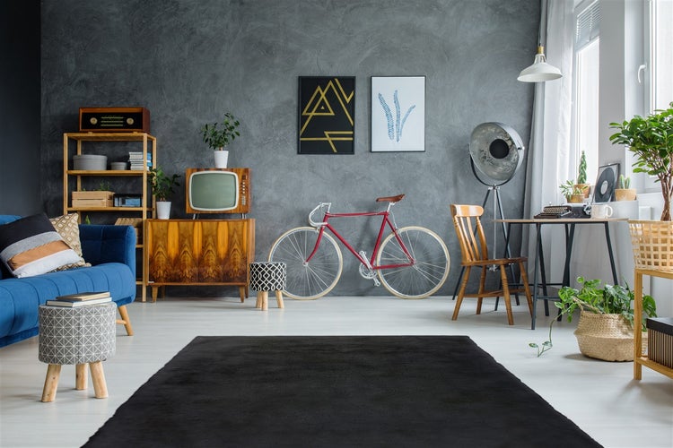 Schwarzer rechteckiger Teppich in einem hellen Zimmer im Vintage-Stil mit blauem Sofa, Holzmöbeln, rotem Fahrrad und dunkelgrauer Wand.