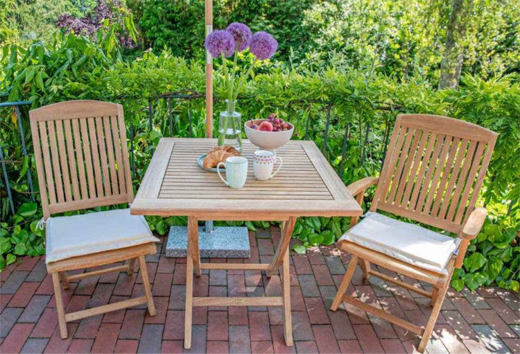 Gartenszene mit Holztisch, zwei Holzstühlen mit Kissen, Blumen und Geschirr