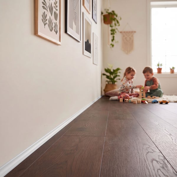 Dunkler Laminatboden mit weißer Fußleiste in einem hellen Kinderzimmer, in dem zwei Kinder auf dem Boden spielen.