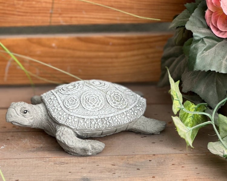 Gartenfigur Schildkröte aus Steinguss auf Holz neben einer Pflanze
