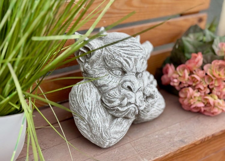 Gartenfigur Wasserspeier aus Stein als dekoratives Element fuer den Aussenbereich auf einer Holzbank.