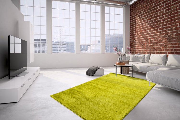 Moderner Wohnbereich im Industriestil mit Backsteinwand, weißem Sofa und leuchtend grünem Hochflor-Teppich auf grauem Boden.