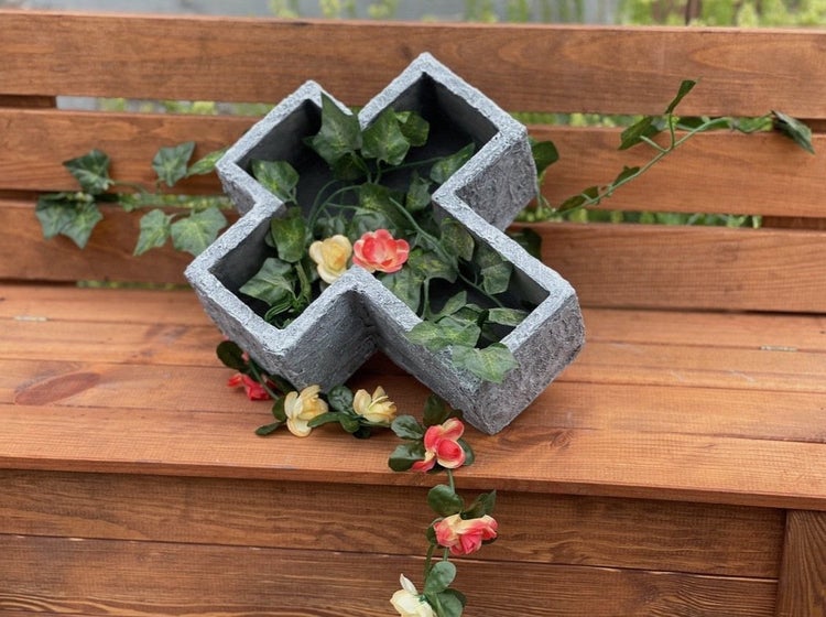 Pflanzschale in Kreuzform aus kunststeinartigem Material auf einer Holzbank mit Efeuranken und Blumen dekoriert