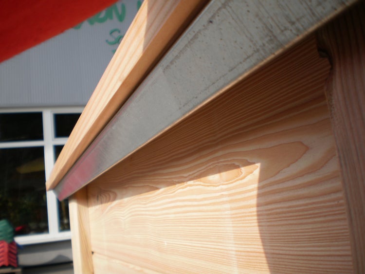 Detailansicht eines Holzhochbeets mit einem metallenen Kantenschutz an der Oberkante.