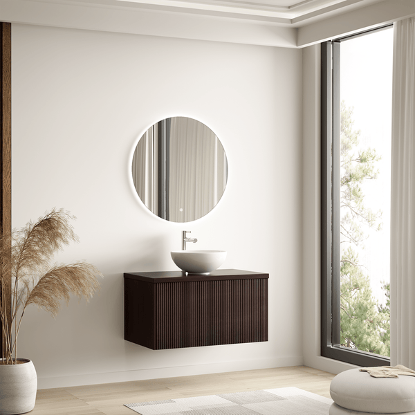 Modernes Badezimmer mit rundem beleuchtetem Spiegel, weißem Aufsatzwaschbecken auf dunklem Holzunterschrank mit Rillenstruktur, helle Atmosphäre.