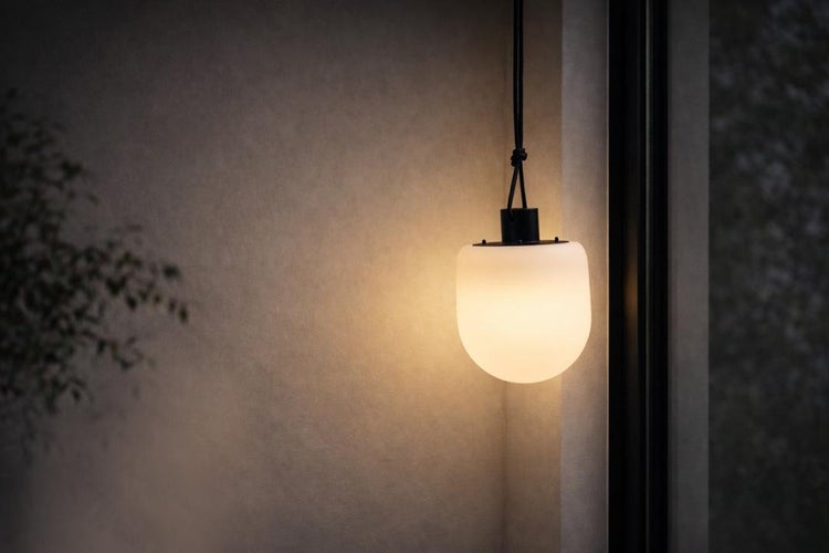 Moderne Außenpendelleuchte mit weißem Schirm und schwarzer Aufhängung, die warmes Licht an eine strukturierte Wand wirft.