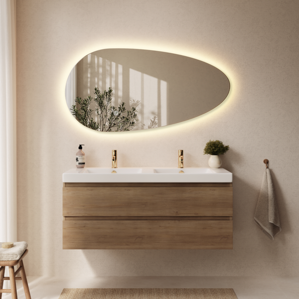 Badezimmer mit organisch geformtem LED Spiegel über einem Doppelwaschtisch mit Holzunterschrank und Armaturen in Metalloptik in einem hellen Raum.