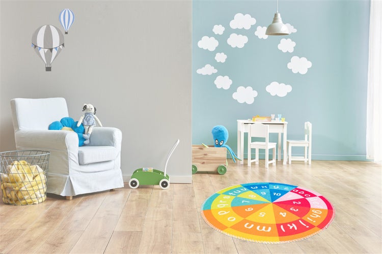 Hell eingerichtetes Kinderzimmer mit einem bunten runden Lernteppich mit Buchstaben und Zahlen auf hellem Bodenbelag in Holzoptik.