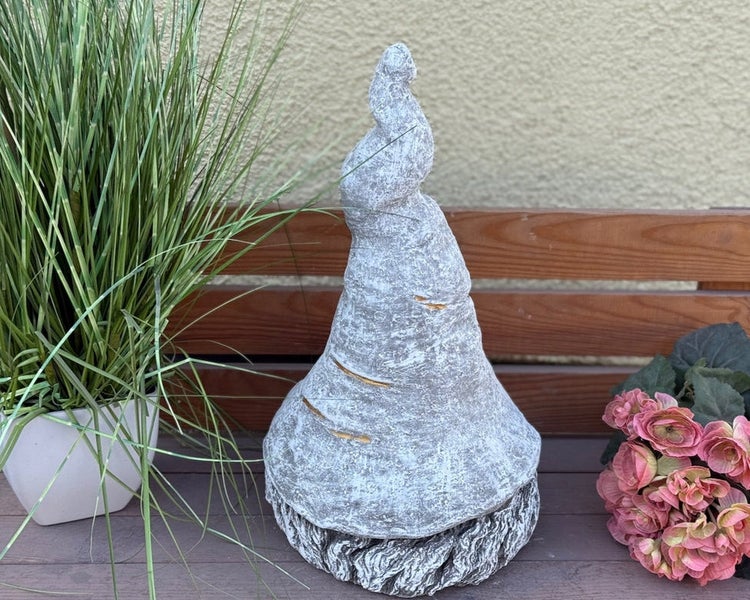 Dekorative Gartenfigur in Form eines stilisierten Gartenzwergs mit großer, strukturierter Zipfelmütze aus Stein auf einer Holzbank.