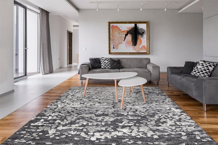 Modernes, helles Wohnzimmer mit abstrakt gemustertem Teppich in Grau und Weiß, grauen Sofas, weißen Beistelltischen und Parkettboden.