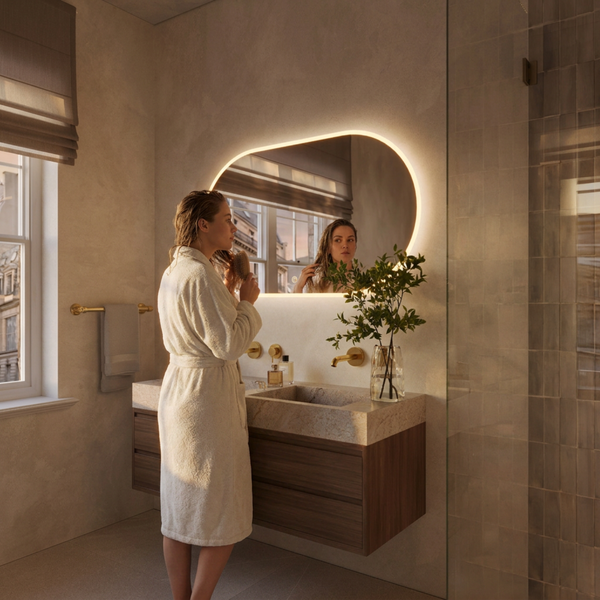Modernes Badezimmer mit Waschtisch aus Holz, organisch geformtem LED Spiegel und einer Frau im Bademantel.