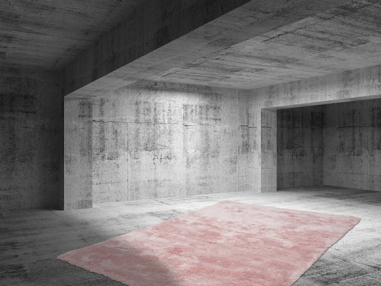 Ein rechteckiger, flauschiger Langflor-Teppich in Rosa liegt auf einem grauen Betonboden in einem modernen, industriell gestalteten Raum.
