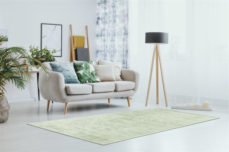 Heller Wohnraum mit hellgrünem Teppich, beigem Sofa mit Kissen und einer Stehleuchte mit Holzstativ.