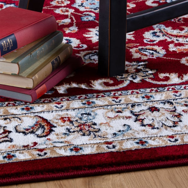 Orientteppich mit floralem Muster und Bordüre, kurzflorig, unter einem Tischbein und Büchern auf einem Holzboden.