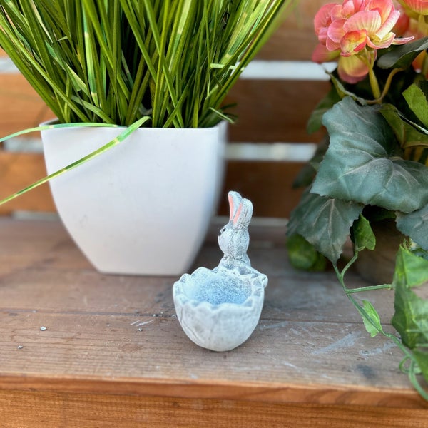 Osterhasenfigur aus Beton in Eierschalenform als Dekoration für den Frühling auf einer Holzoberfläche.
