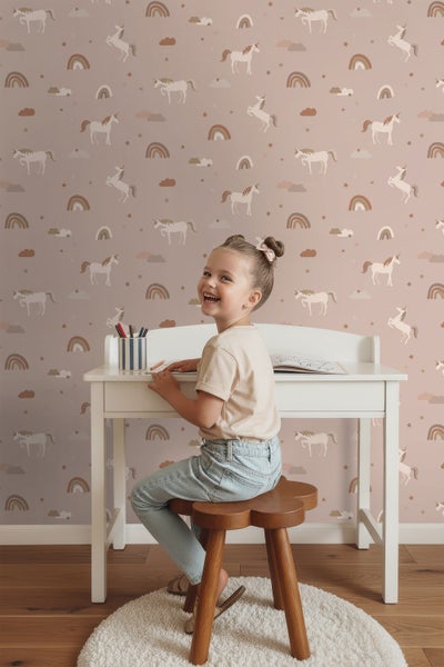 Mädchen am weißen Schreibtisch vor einer Kinderzimmer Tapete mit Einhorn Muster