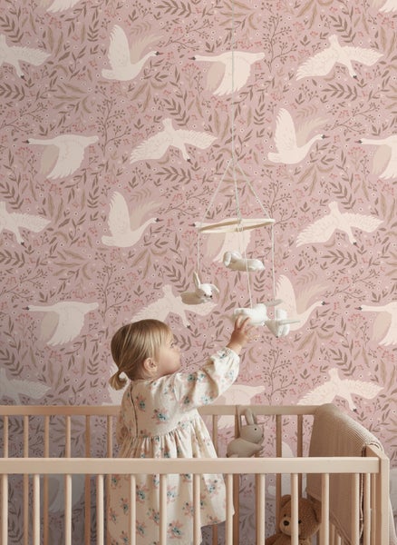 Mädchen im Kinderbett mit Mobile vor einer Tapete mit Schwanenmuster