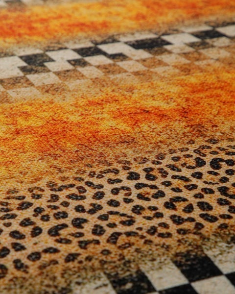 Nahaufnahme eines Teppichs mit verschiedenen Mustern wie Leopardenmuster, Karodesign und einer strukturierten orange-gelben Oberfläche.