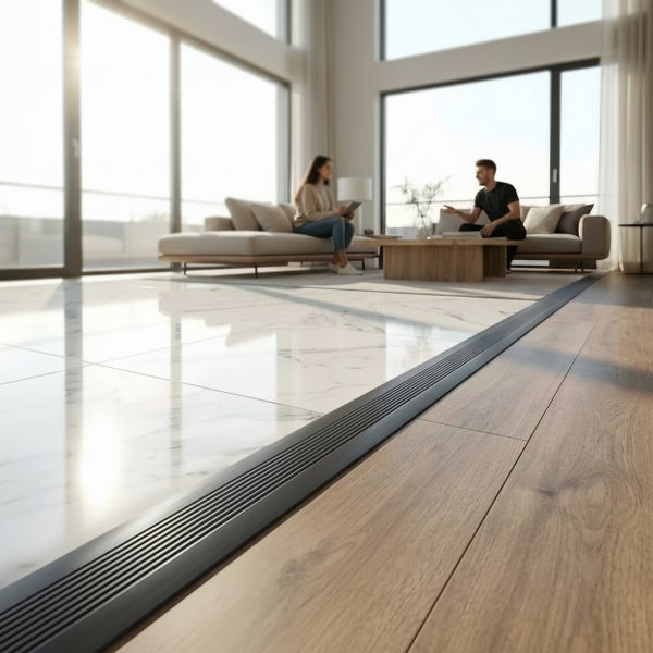 Übergangsprofil zwischen Fliesen mit Marmoroptik und Holzdielen in einem hellen, modernen Wohnzimmer mit zwei Personen auf einem Sofa im Hintergrund.
