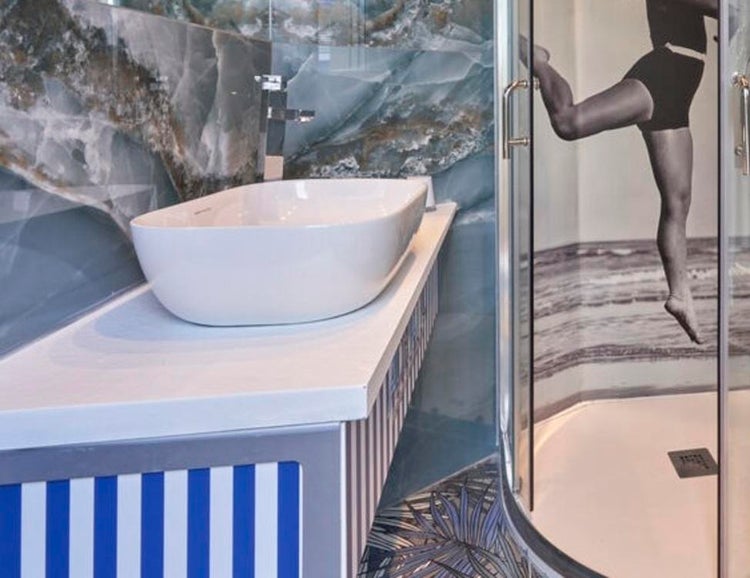 Modernes Badezimmer mit weißem Aufsatzwaschbecken auf einer Platte, daneben eine Dusche mit einer Duschkabine mit grafischem Aufdruck.