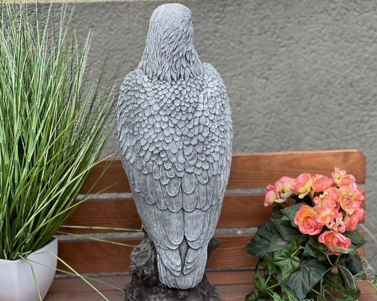 Gartenfigur eines Adlers aus Steinguss, Rückansicht auf einer Holzbank stehend neben Pflanzen