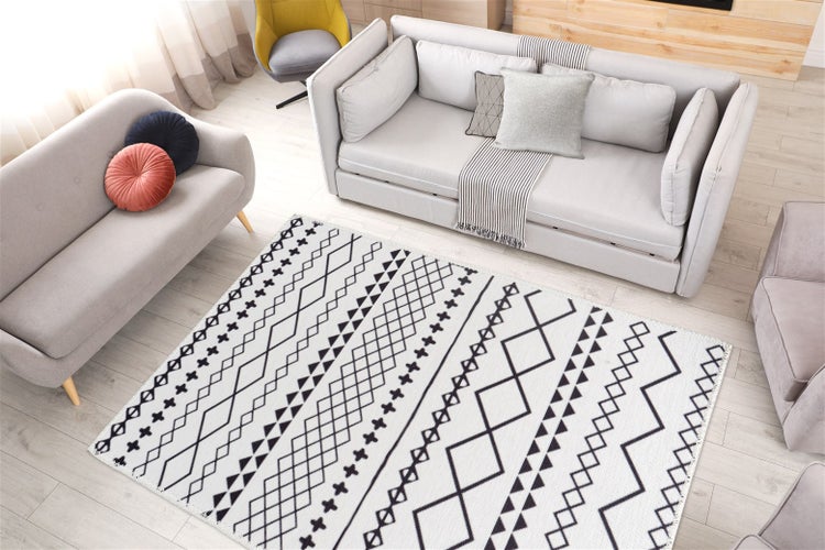 Heller, modern eingerichteter Wohnraum mit grauen Sofas und einem schwarz-weißen Teppich mit geometrischem Muster auf hellem Holzboden.