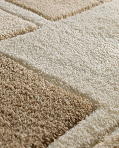 Detailaufnahme eines weichen Hochflor-Teppichs mit geometrischem Muster in Beige und Creme.