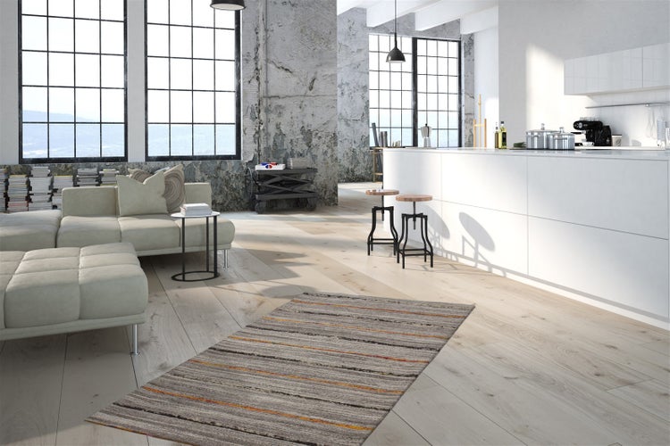 Helles Loft im Industriedesign mit hellem Bodenbelag in Holzoptik, weißer Kücheninsel und modernem Wohnbereich mit Sofa und Teppich.