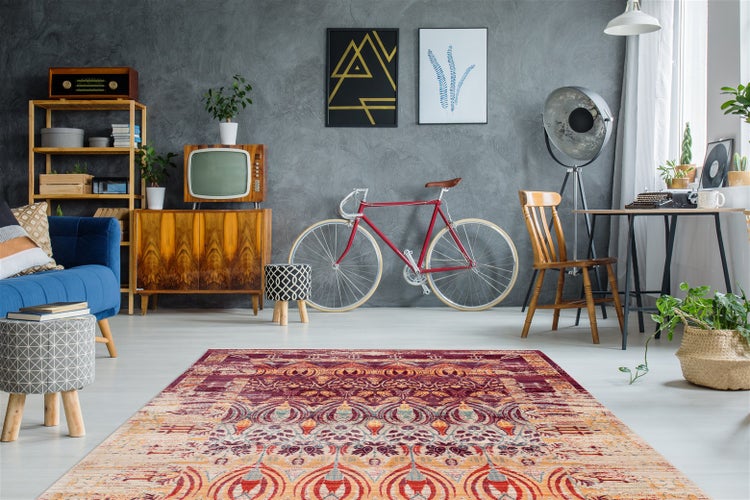 Heller Wohnraum im Retro-Stil mit buntem Orientteppich, blauem Sofa, Vintage-Holzmöbeln, Fahrrad an grauer Wand und hellem Boden.