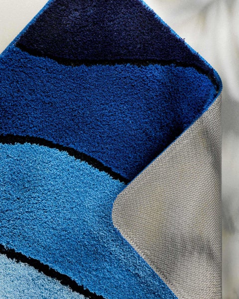 Detailaufnahme einer flauschigen Badematte mit wellenförmigem blauem Muster und rutschhemmender Rückseite.